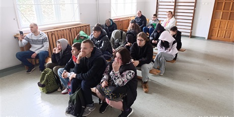 Powiększ grafikę: Grupa uczniów siedząca na ławkach na sali gimnastycznej, oglądają i słuchają występu wokalistek.